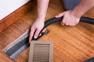 Person cleaning an air duct on through the vent in the wood floor.