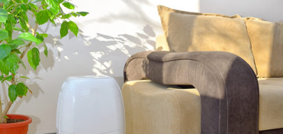 A portable dehumidifier placed next to a couch in a living room to collect water from the air
