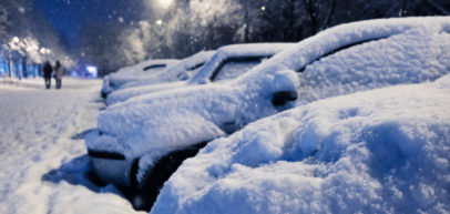 A row of parked cars in a parking lot covered in a thick blanket of snow at nightfall